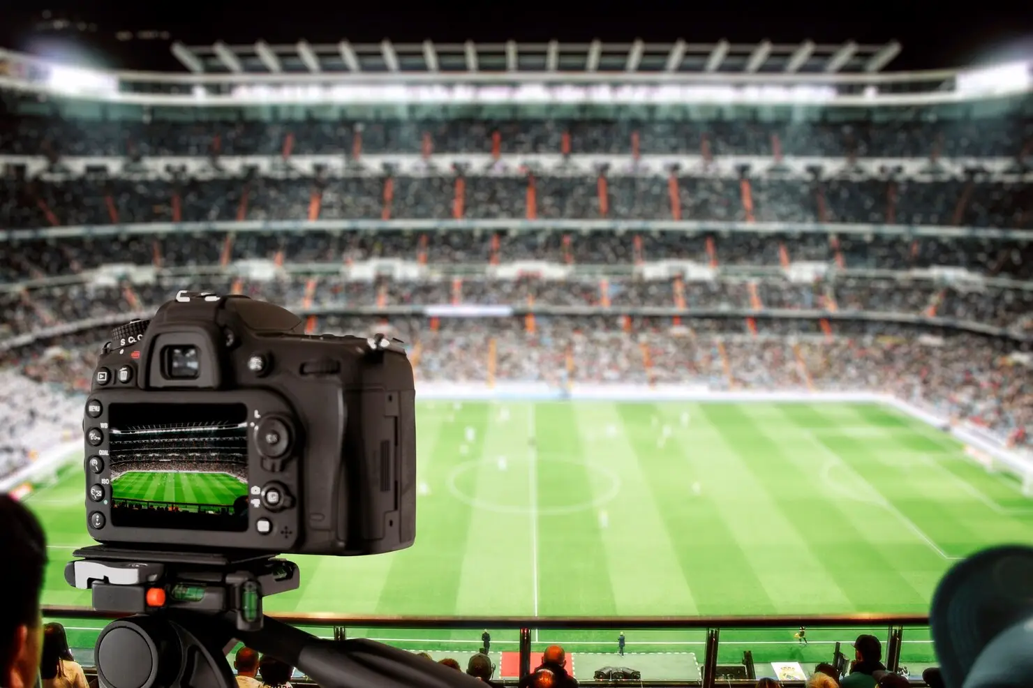 Camera on tripod capturing soccer match in crowded stadium under bright lights