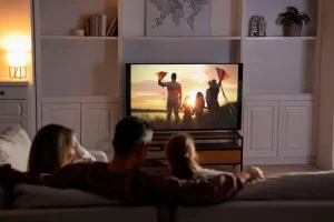 Family watching sunset scene on television in cozy living room with warm lighting