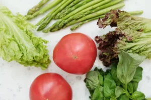 Fresh tomatoes, asparagus, and assorted leafy greens on a marble surface