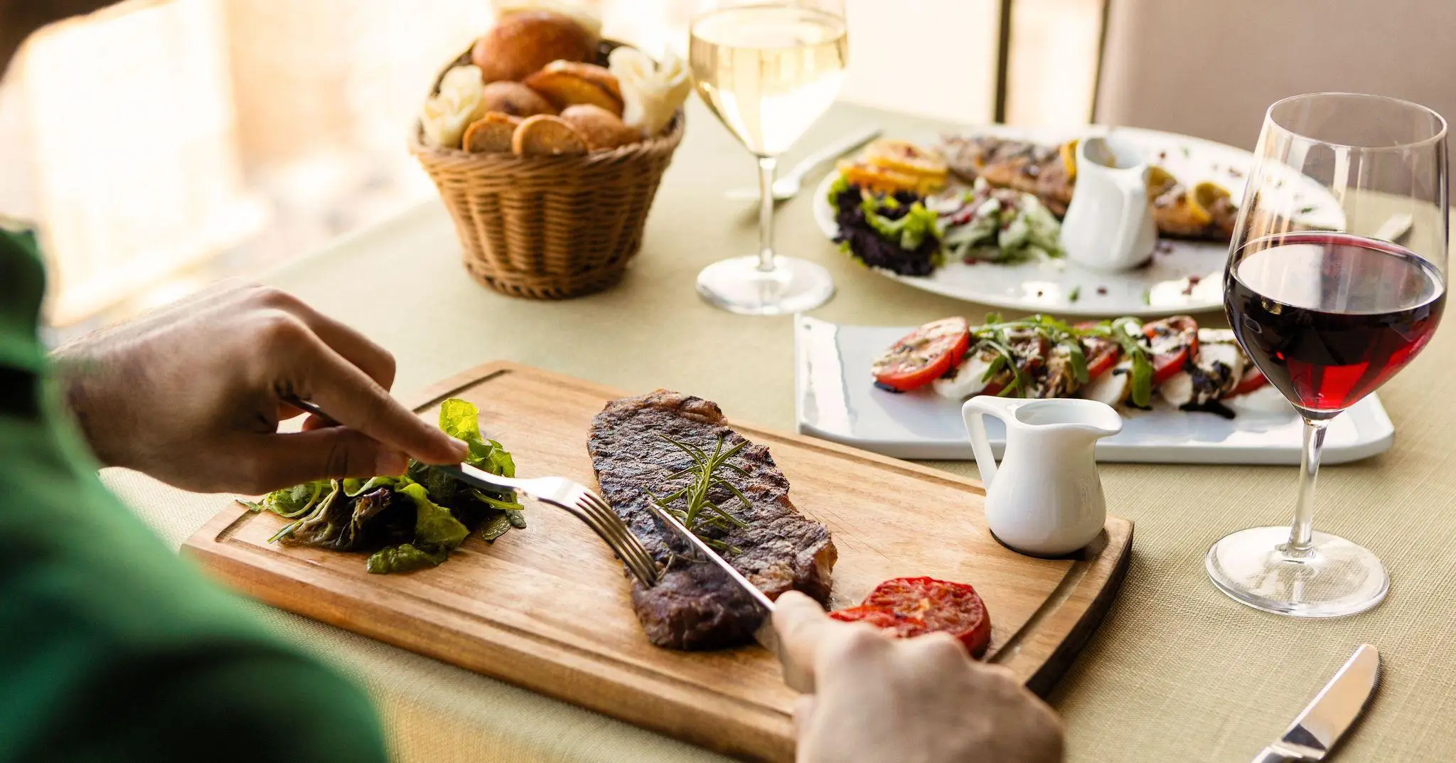 Steak being cut on wooden board with salad and wine in elegant dining setting