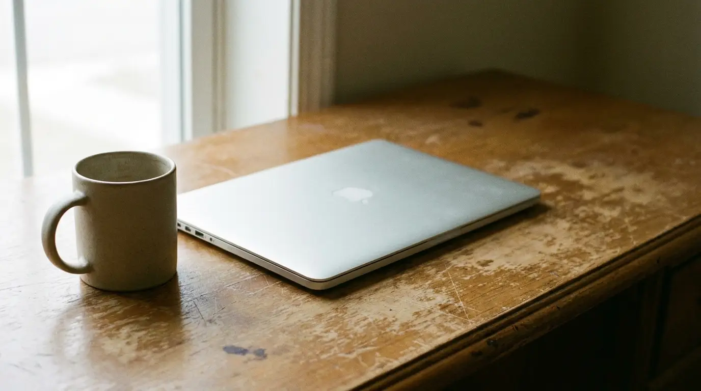 Laptop and ceramic mug on rustic wooden desk near window in natural light