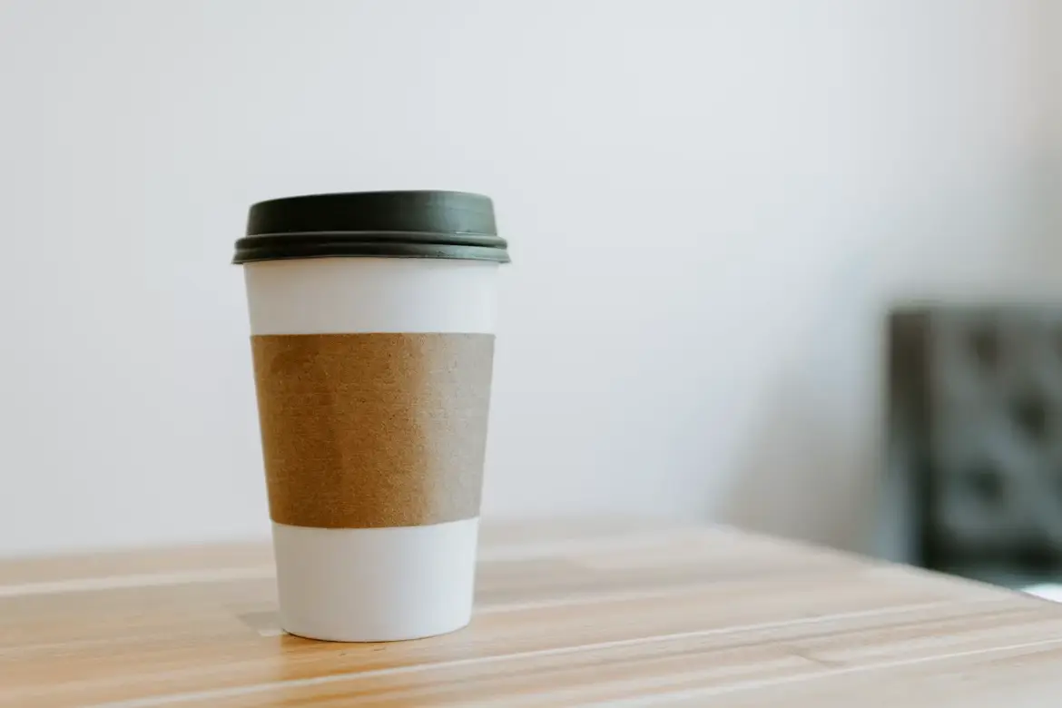 Disposable coffee cup with black lid on light wooden table in minimal indoor setting