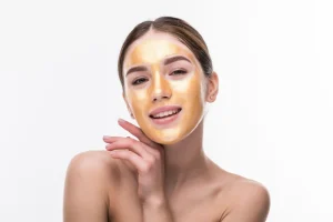 Woman with gold facial mask smiling in bright studio setting