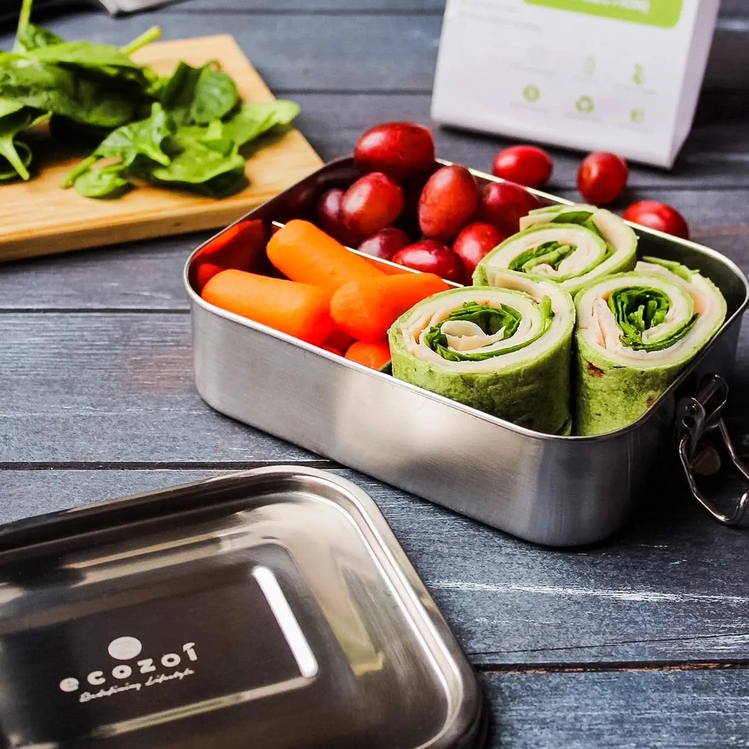 Stainless steel lunchbox with wraps, baby carrots, and grapes on wooden table