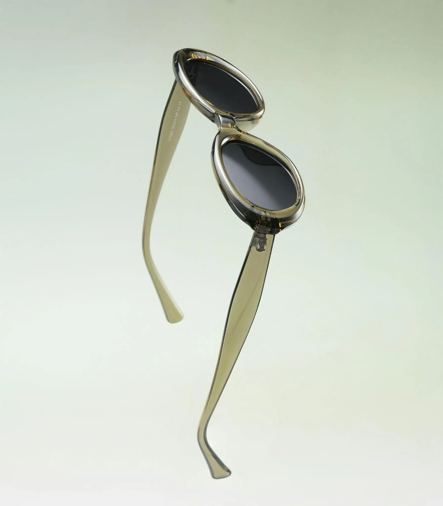 Stylish round brown sunglasses with sleek transparent frames on light green background