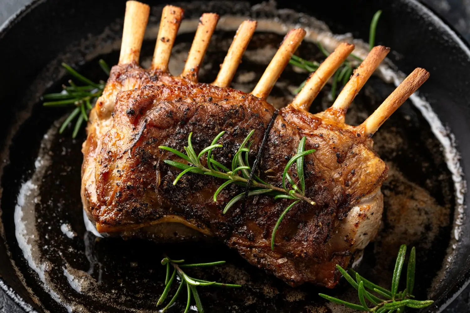 Rack of lamb with rosemary sprigs sizzling in a cast iron skillet