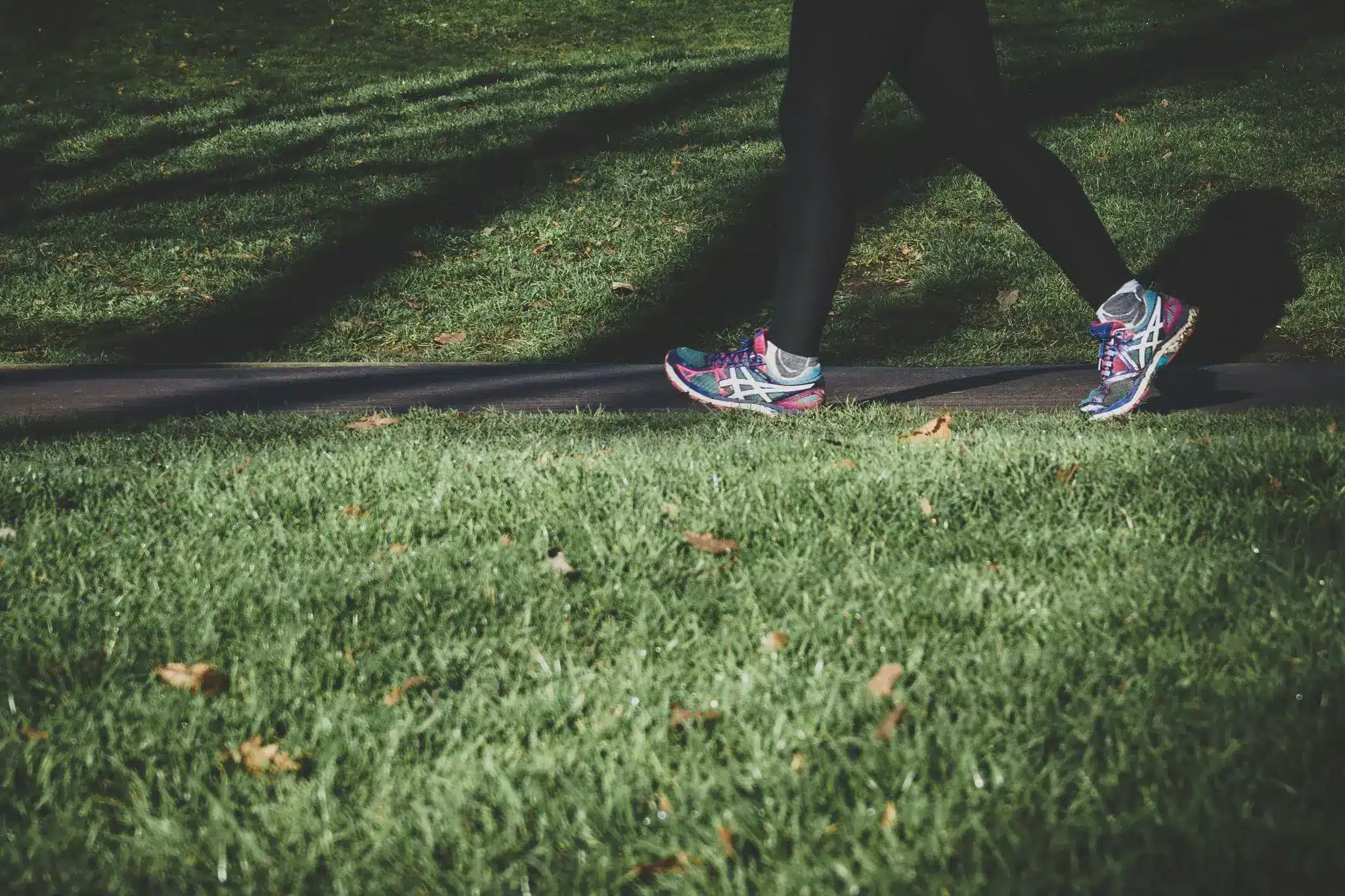 Person walking on a park path wearing colorful athletic shoes and black leggings