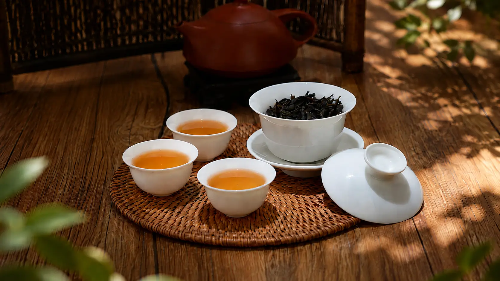 Ceramic teacups and teapot on woven mat in sunny wooden setting