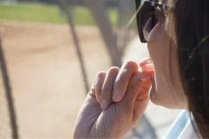 Person wearing sunglasses eating candy near a baseball field on a sunny day