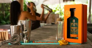 Bartending tools and orange box with bottle on bar counter, people shaking cocktails in background