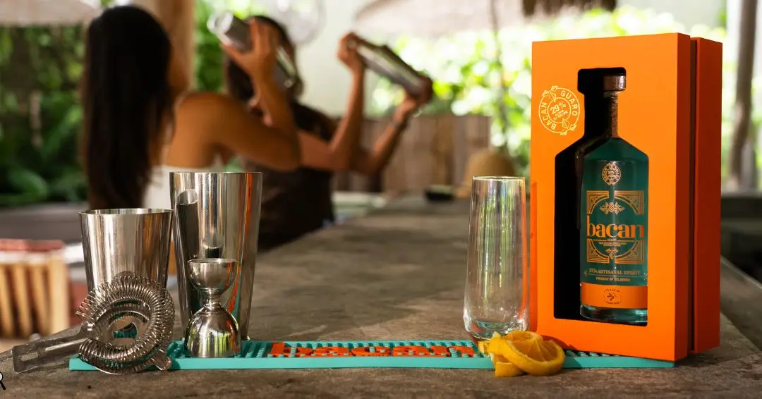 Bartending tools and orange box with bottle on bar counter, people shaking cocktails in background