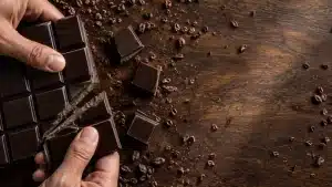Breaking dark chocolate bar with cocoa nibs on wooden surface