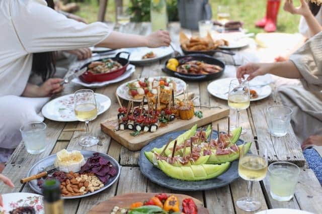 Outdoor picnic with assorted appetizers and wine on wooden table surrounded by people
