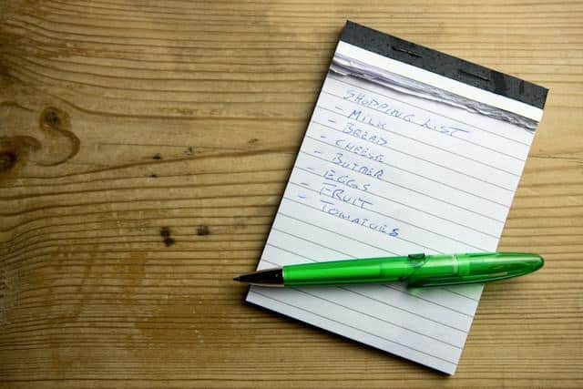 Shopping list on notepad with green pen on wooden surface