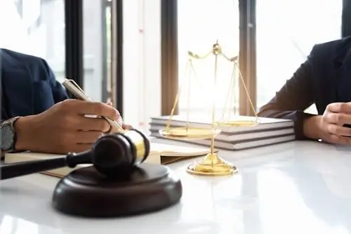 Gavel and golden scales on desk with person writing in bright office setting
