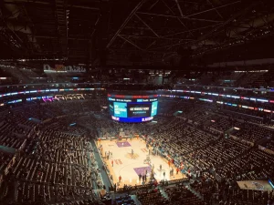 Basketball game in a large indoor arena with bright scoreboard and audience seating