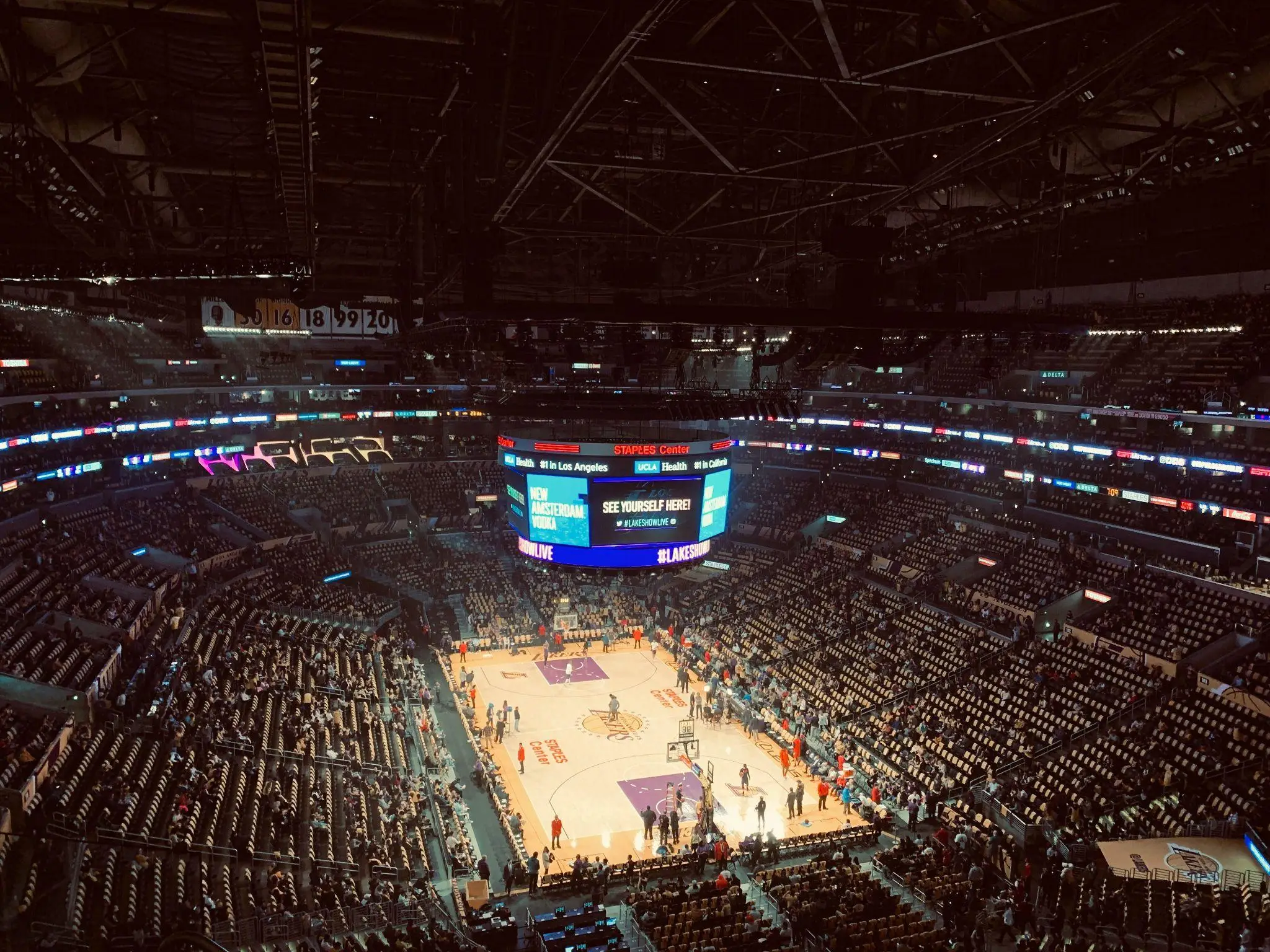 Basketball game in a large indoor arena with bright scoreboard and audience seating