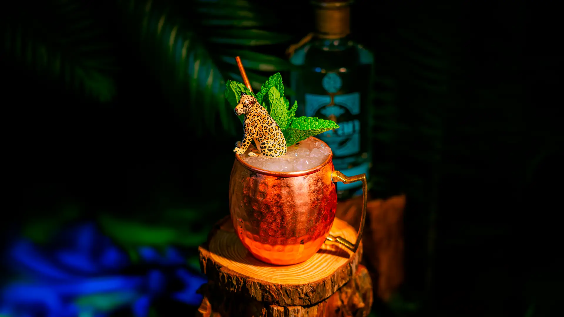 Copper mug cocktail with mint leaves and leopard figurine on ice in dimly lit setting
