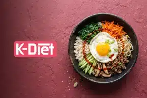 Korean bibimbap with fried egg, vegetables, and rice in a black bowl on textured red background