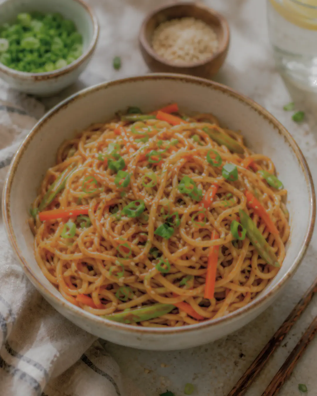 Stir-fried noodles with sliced carrots and green onions in a ceramic bowl on a textured cloth