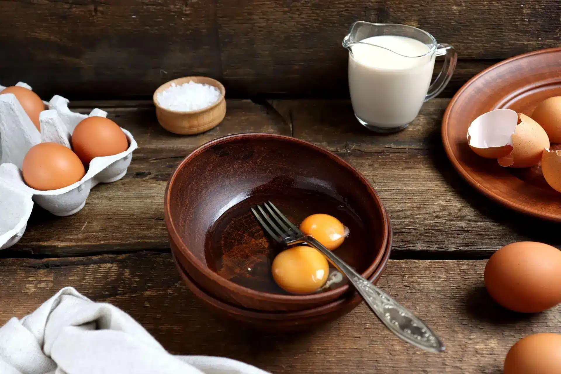 Eggs and milk on rustic wooden table with cracked eggshells and mixing bowl