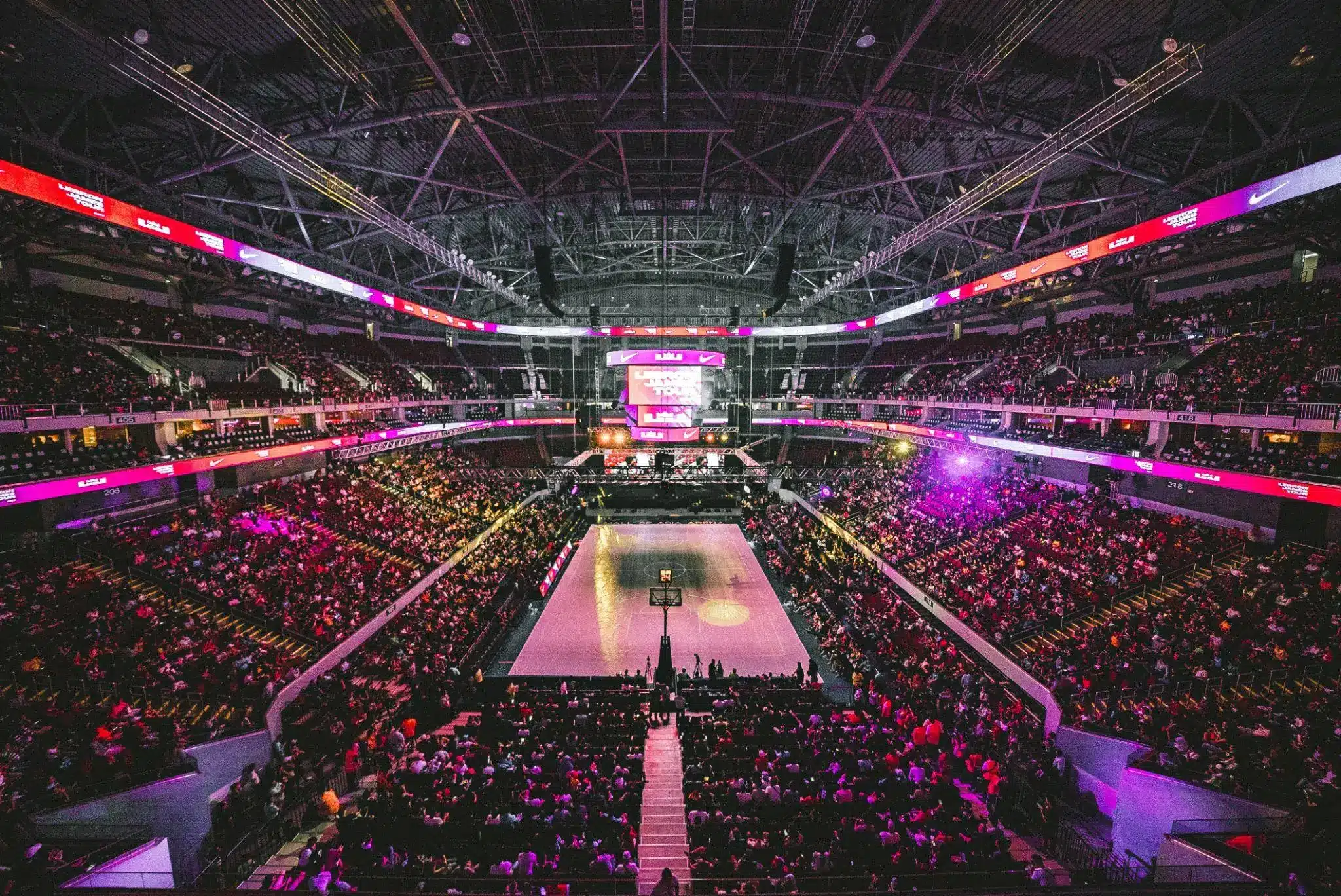 Crowded indoor stadium with colorful lighting focused on central basketball court
