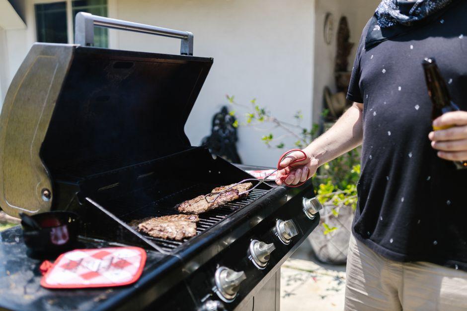 Man grilling steak on outdoor gas grill in sunny patio setting