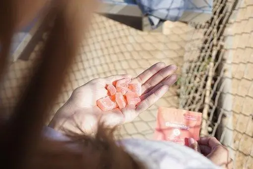 Hands holding several orange gummies with open package at a beach setting