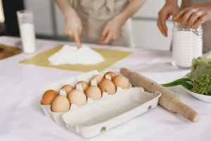 Carton of eggs with rolling pin and flour on kitchen counter