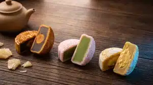 Three mooncakes with different fillings on a wooden table beside a brown teapot