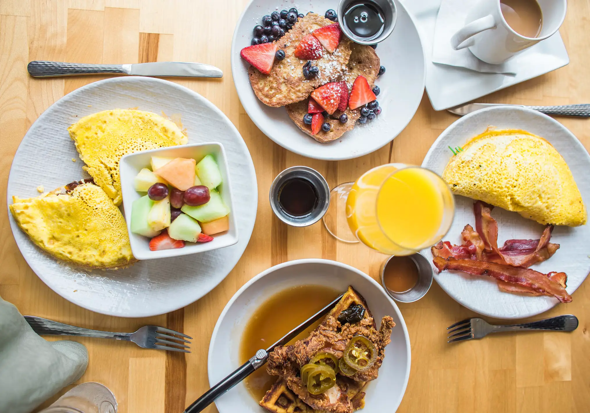 Breakfast spread with omelets, pancakes, fried chicken and waffles, bacon, fruit salad, and orange juice