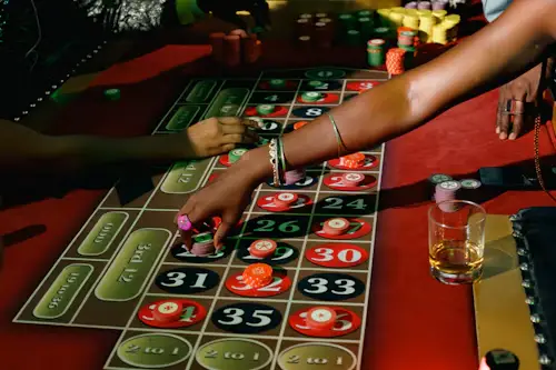 Hands placing bets on a roulette table with colorful chips in a dimly lit casino