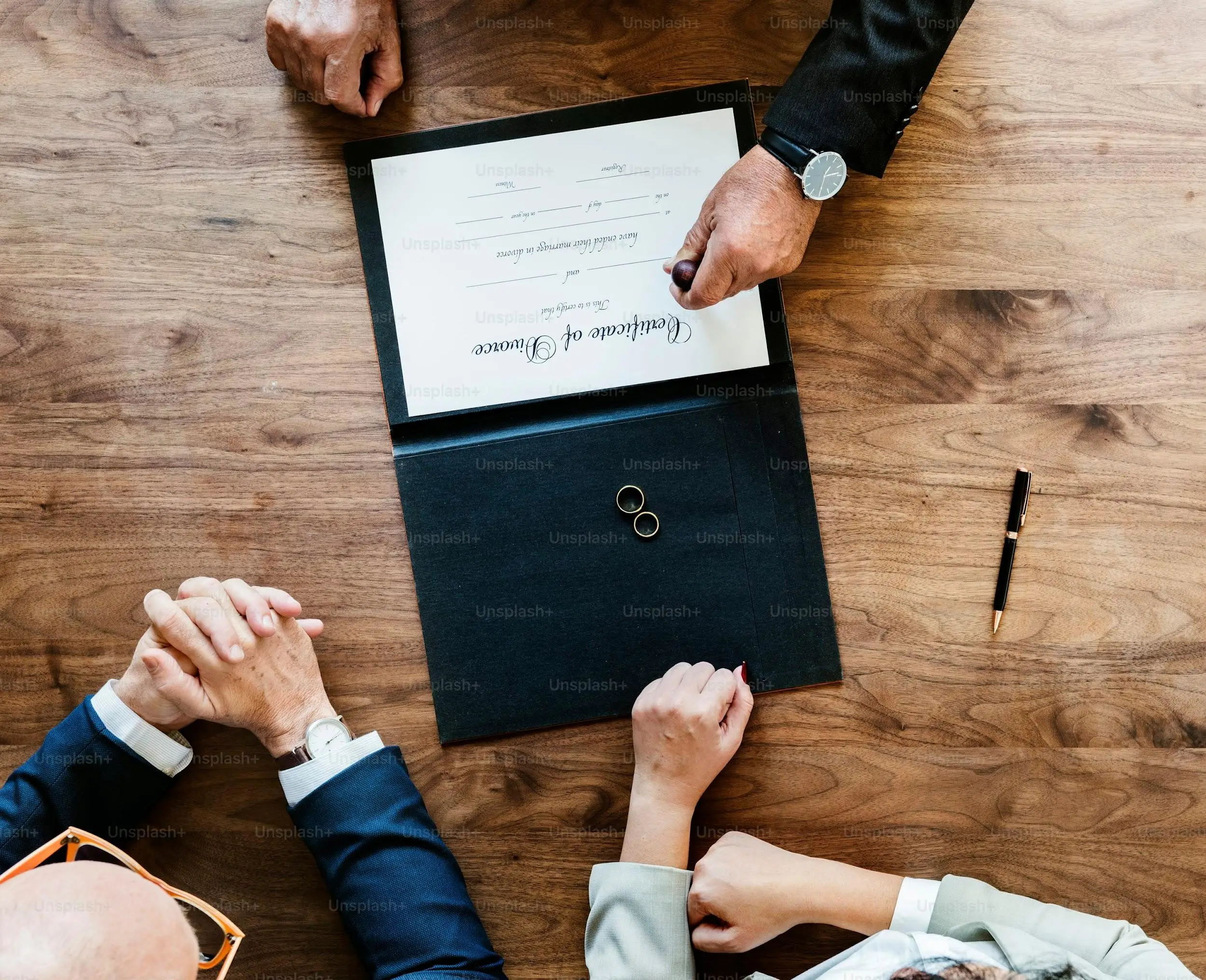 Divorce decree with wedding rings and hands on wooden table in office setting
