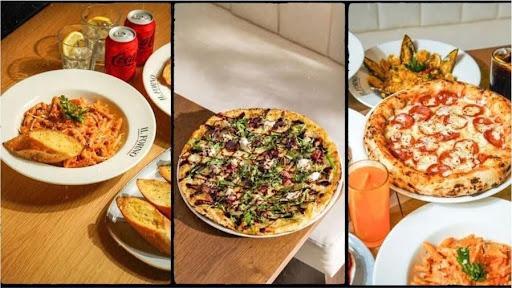 Assorted pizzas and pasta dishes on wooden tables with garlic bread and drinks