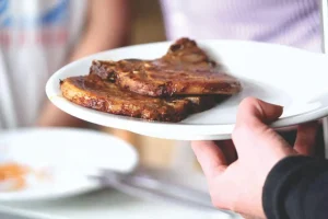 Grilled pork chops on white plate held by person in casual indoor setting