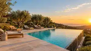 Infinity pool with lounge chairs surrounded by olive trees during sunset in outdoor setting