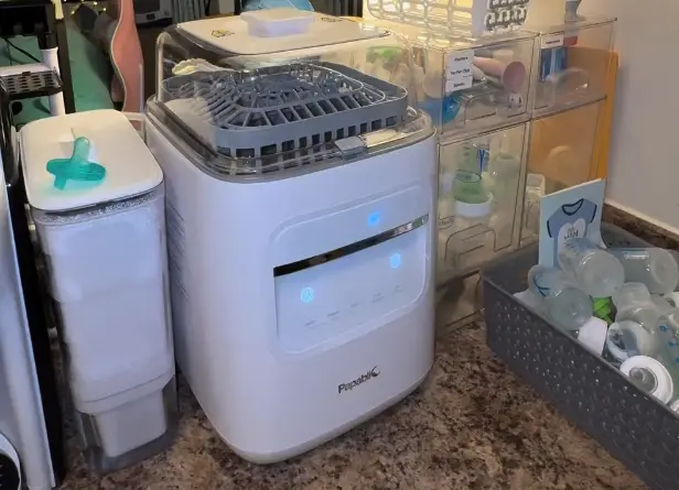 Baby bottle sterilizer on kitchen counter with pacifiers and baby accessories nearby