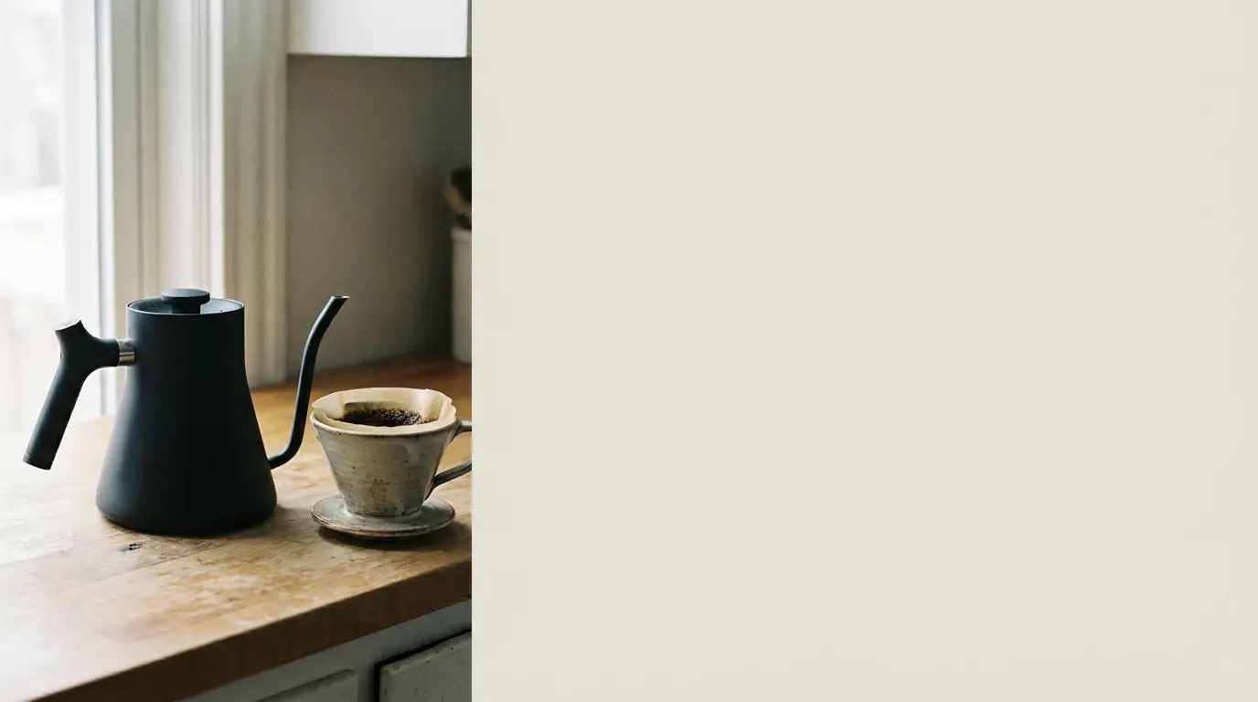 Black kettle and ceramic dripper on wooden kitchen countertop near window
