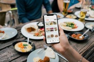 Hand holding smartphone displaying food delivery app at outdoor dining table with various dishes