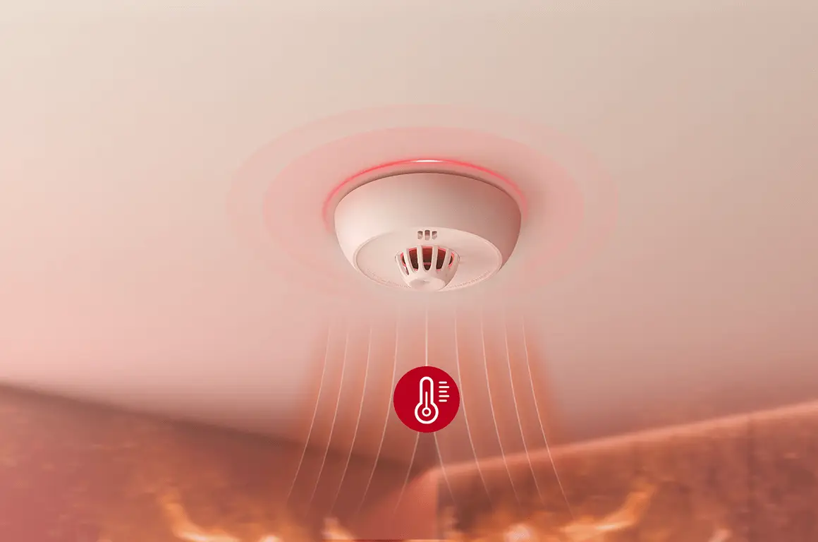 Ceiling-mounted smoke detector emitting red light in a warm-toned indoor environment