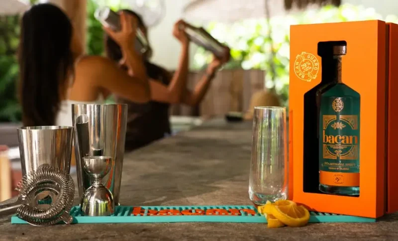 Bartending tools and orange box with bottle on bar counter, people shaking cocktails in background