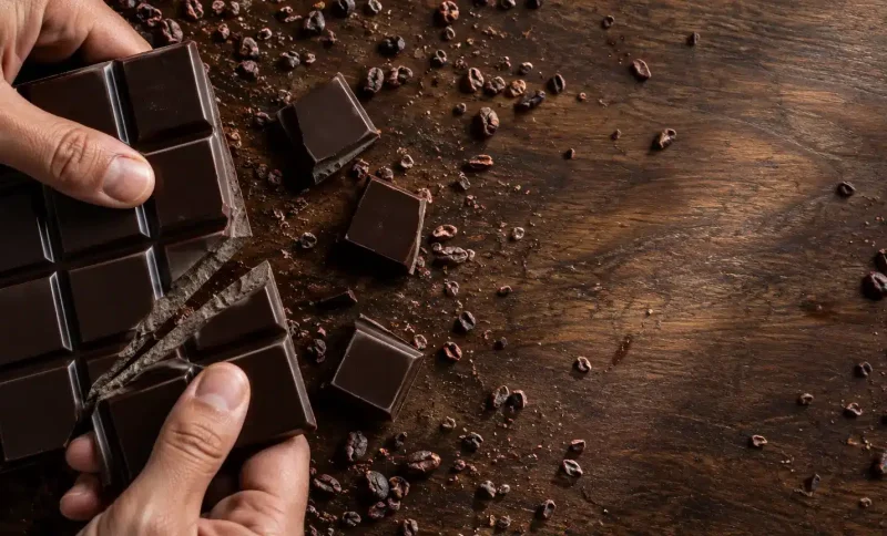 Breaking dark chocolate bar with cocoa nibs on wooden surface