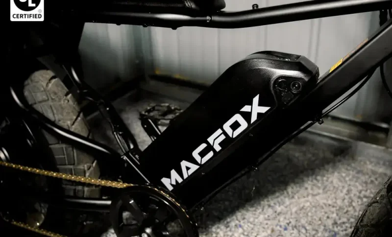 Electric bike frame with visible battery and thick treaded tires in a dim garage setting