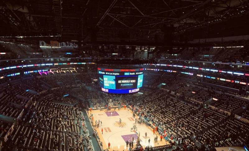 Basketball game in a large indoor arena with bright scoreboard and audience seating