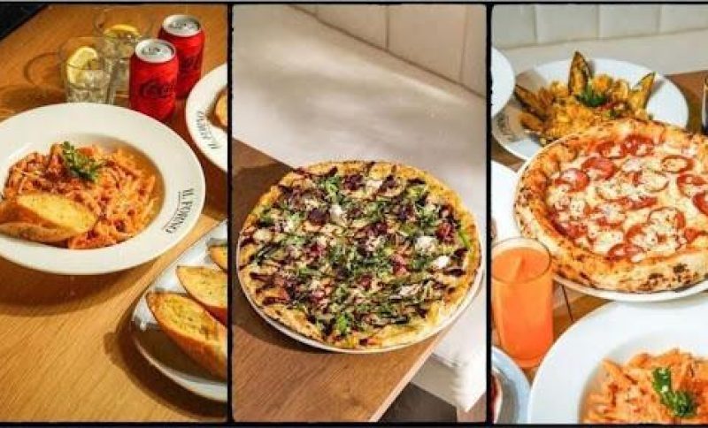 Assorted pizzas and pasta dishes on wooden tables with garlic bread and drinks