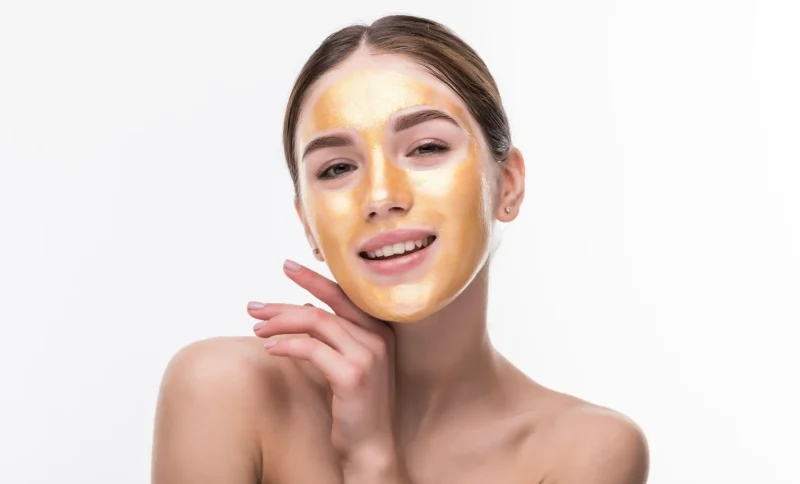 Woman with gold facial mask smiling in bright studio setting