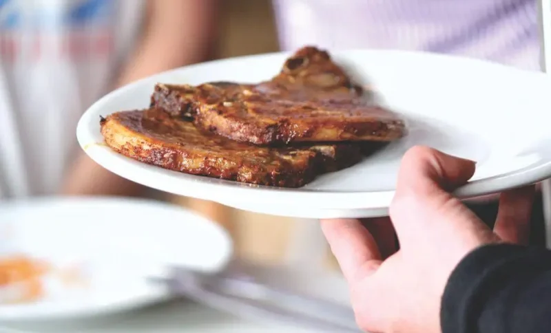 Grilled pork chops on white plate held by person in casual indoor setting