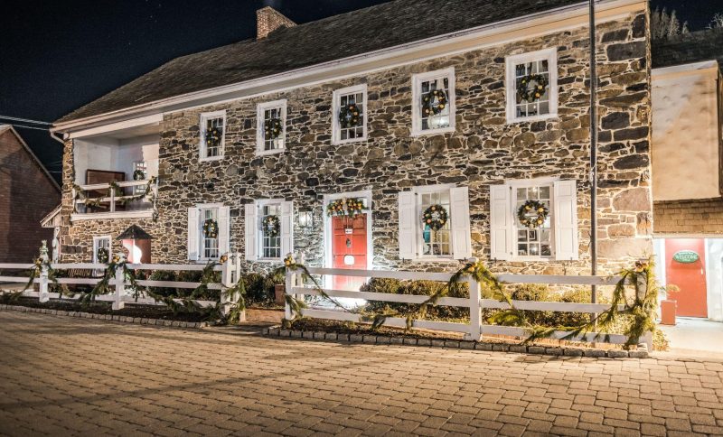 Historic stone building with holiday wreaths and garlands at night, warm lighting and cobblestone path