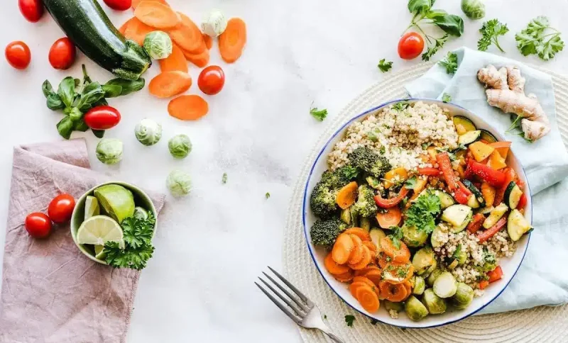 Quinoa and roasted vegetables in a bowl with fresh ingredients on a white surface