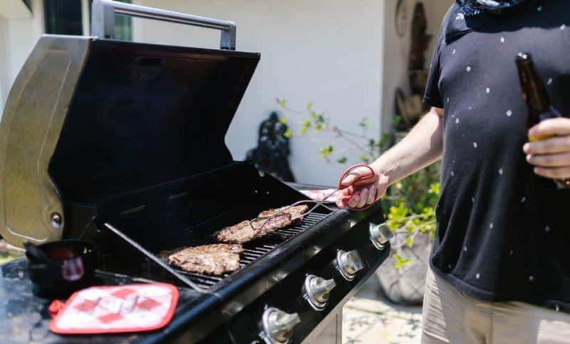 Man grilling steak on outdoor gas grill in sunny patio setting
